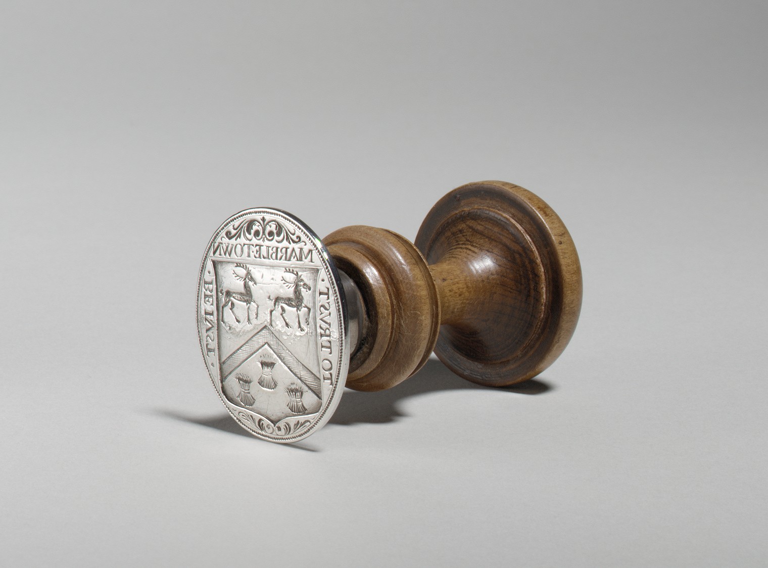 Silver seal matrix with a turned wooden handle and engraved arms.